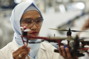 Researcher wearing safety glasses and a lab coat closely examining a drone's propeller and rotor components.