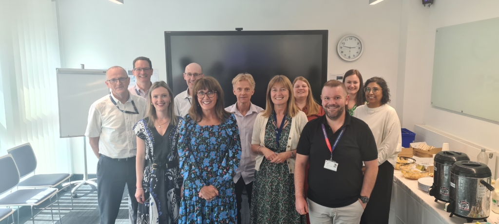 Group photo of colleagues posing together in a meeting room with refreshments set up nearby.