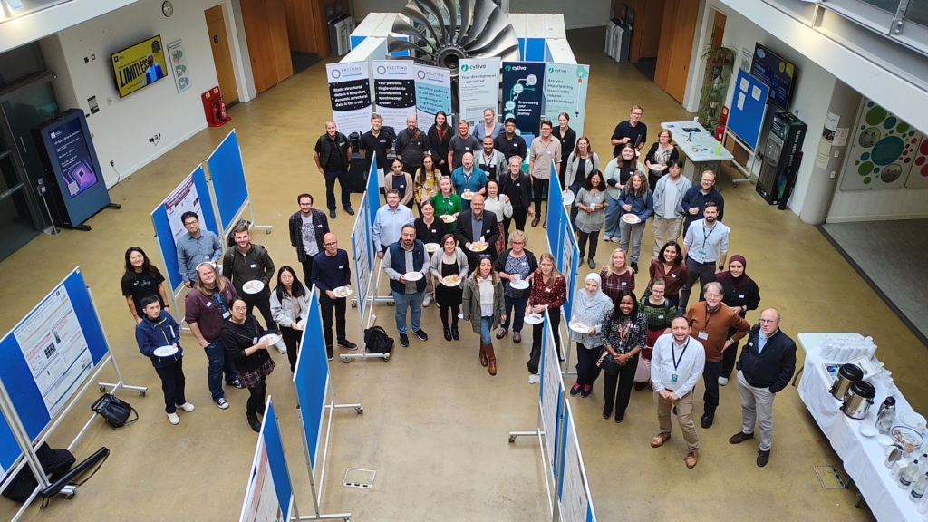 Aerial group photo of attendees at a Biophysics research poster session, standing between exhibition boards.