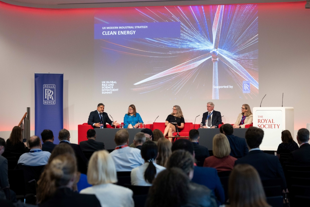Panel discussion at the UK Global R&D and Science Summit, with speakers seated in front of a "UK Modern Industrial Strategy – Clean Energy" slide, with a Rolls-Royce banner, and a Royal Society lectern to either side of them.